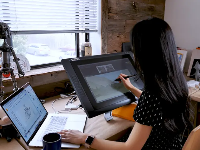 girl sitting at a desk working on a laptop and drawing tablet