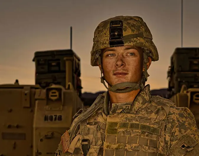 soldier looking at camera in front of military vehicle