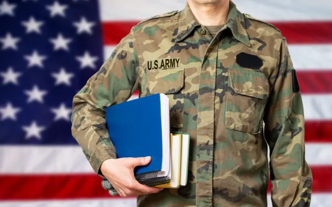 military student holding books in front of American flag